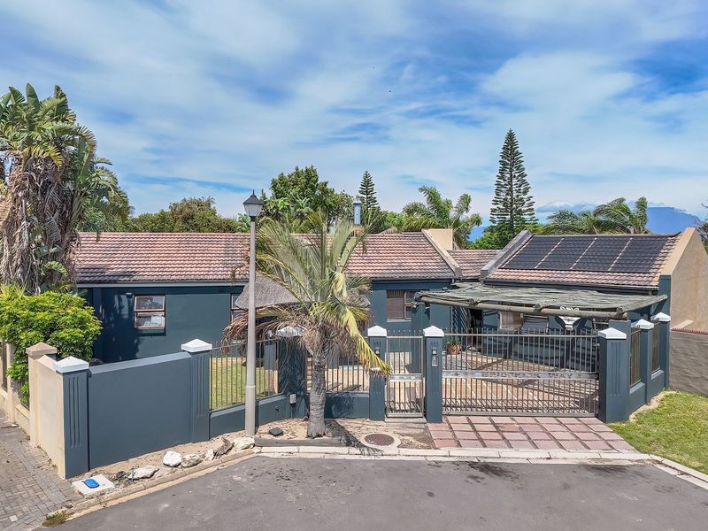 Front exterior view of the property featuring a paved driveway, secure metal gate, perimeter wall, and roof-mounted solar panels.