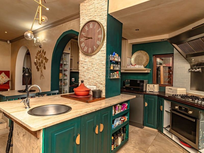 A characterful kitchen featuring a central island with stone countertop, built-in gas hob, oven, and extractor fan, accented by deep green cabinetry and stone-clad pillars.
