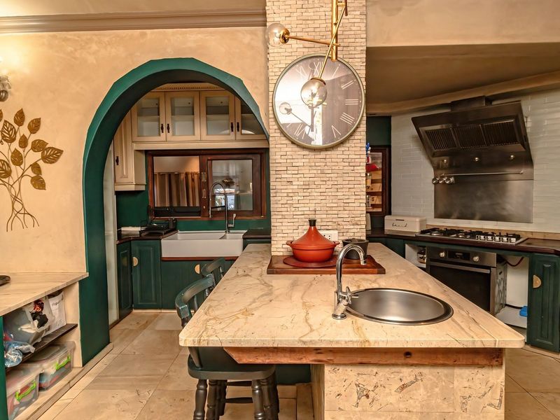 A characterful kitchen featuring a central stone-topped island, farmhouse sink, built-in oven with gas hob, and custom cabinetry with an arched entryway.