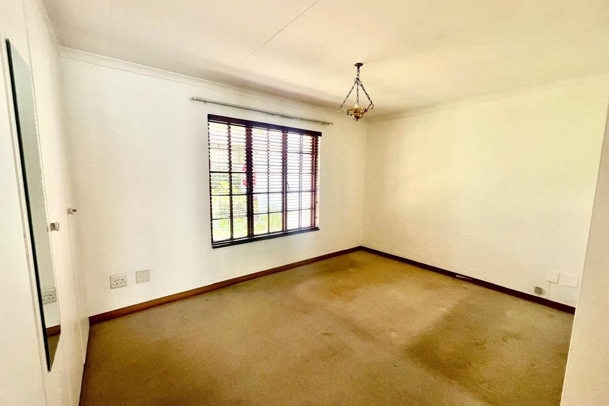 An empty bedroom featuring neutral walls, a built-in cupboard, and a window with venetian blinds. The room requires new flooring to refresh the space.