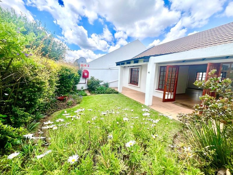 A well-maintained rear garden featuring a tiled patio, established greenery, and timber-framed glass doors leading into the residence.