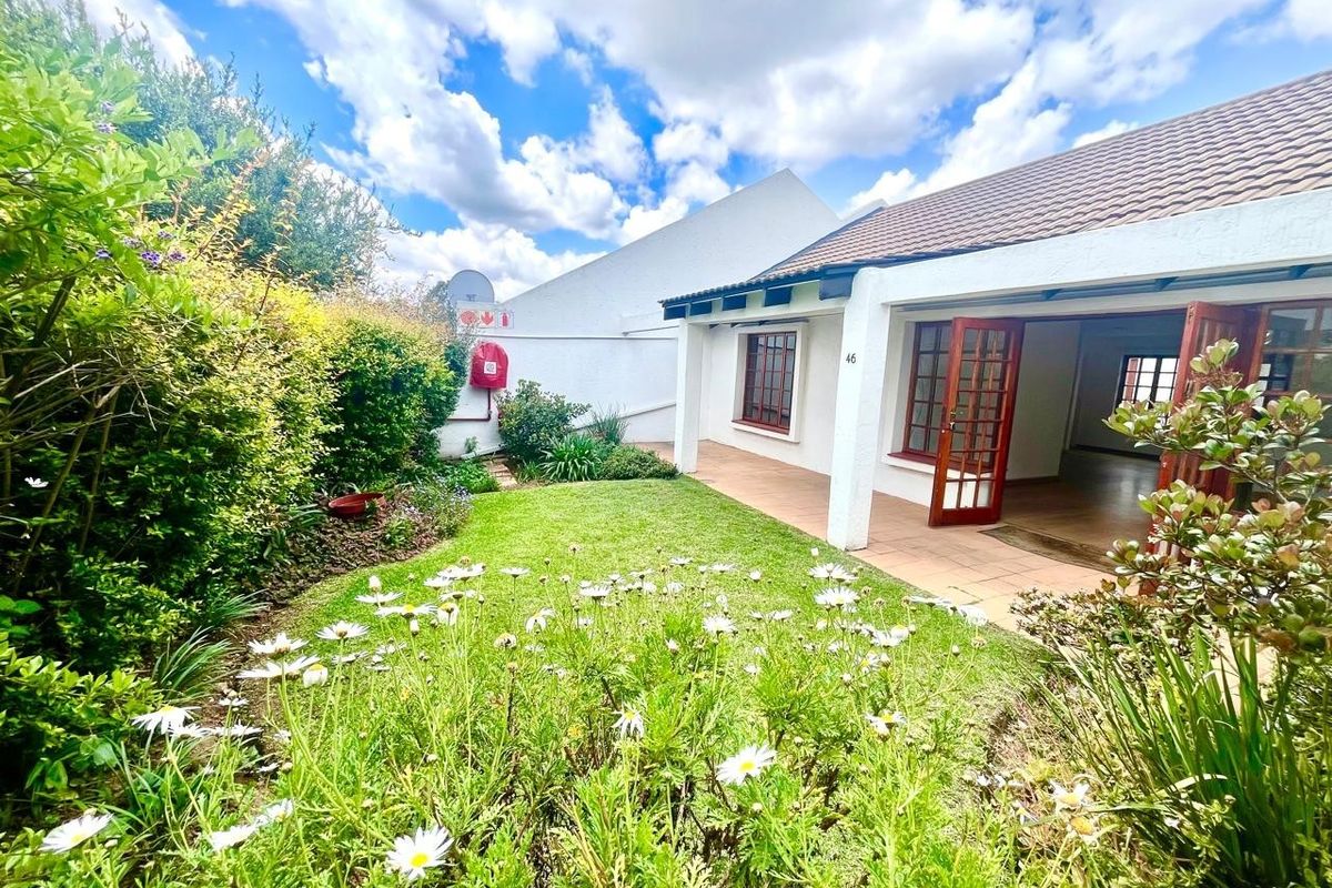 A well-maintained rear garden featuring a tiled patio, established greenery, and timber-framed glass doors leading into the residence.