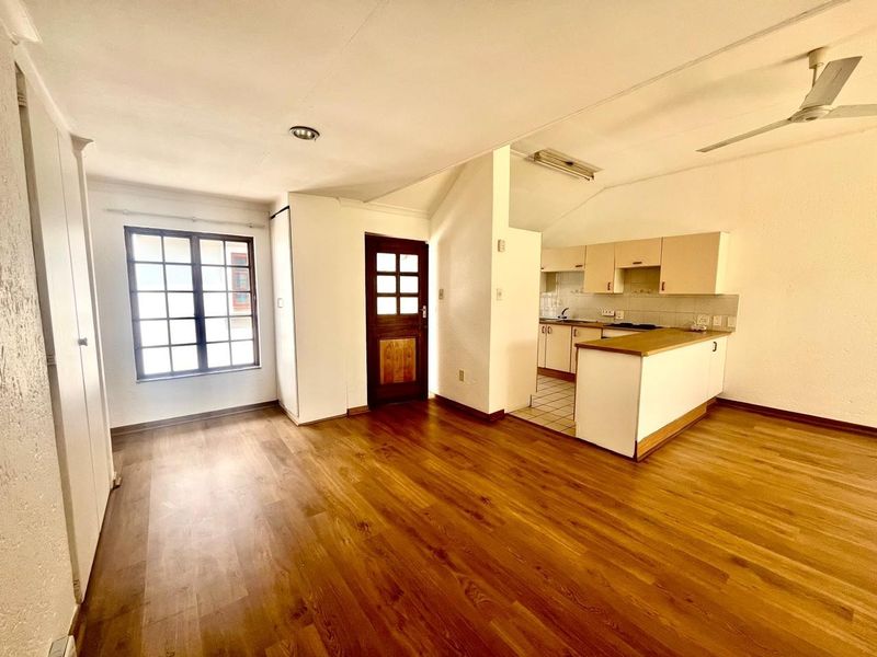 Open plan living area featuring laminate flooring, a ceiling fan, and a functional kitchen with built-in cabinetry and a peninsula counter.