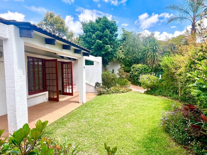 A well-maintained rear garden featuring a tiled patio area, established landscaping, and classic french doors leading into the residence.