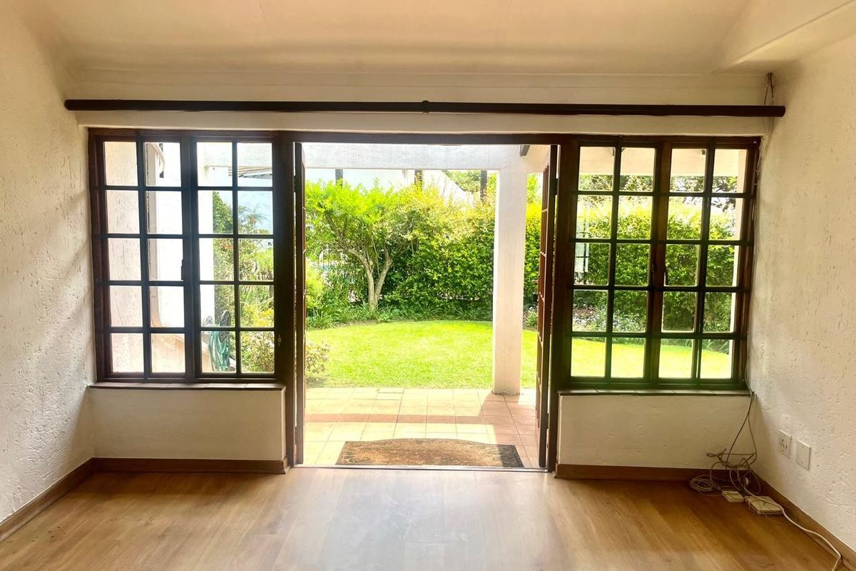 Bright living area featuring timber-framed french doors opening onto a private patio and garden, with laminate flooring and neutral walls.