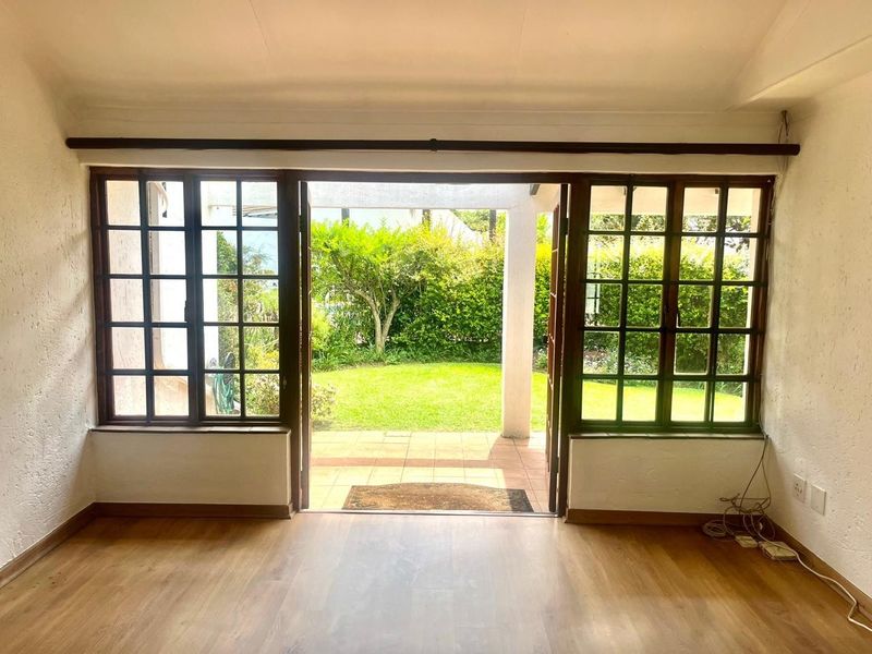 Bright living area featuring timber-framed french doors opening onto a private patio and garden, with laminate flooring and neutral walls.