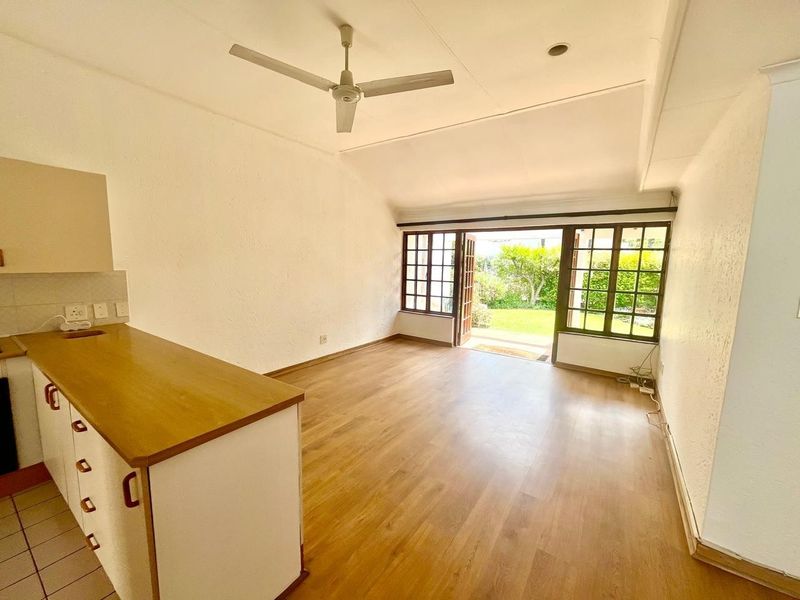 Open-plan living area featuring laminate flooring, a ceiling fan, and timber-framed glass doors opening to a private garden.