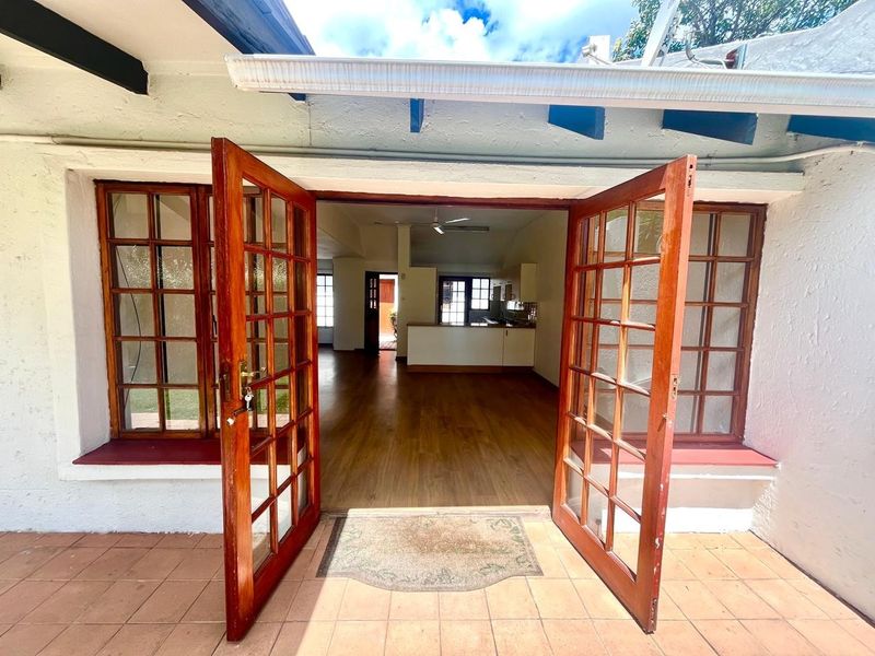 A view from the tiled patio through open timber french doors into an open-plan living and kitchen area with laminate flooring.