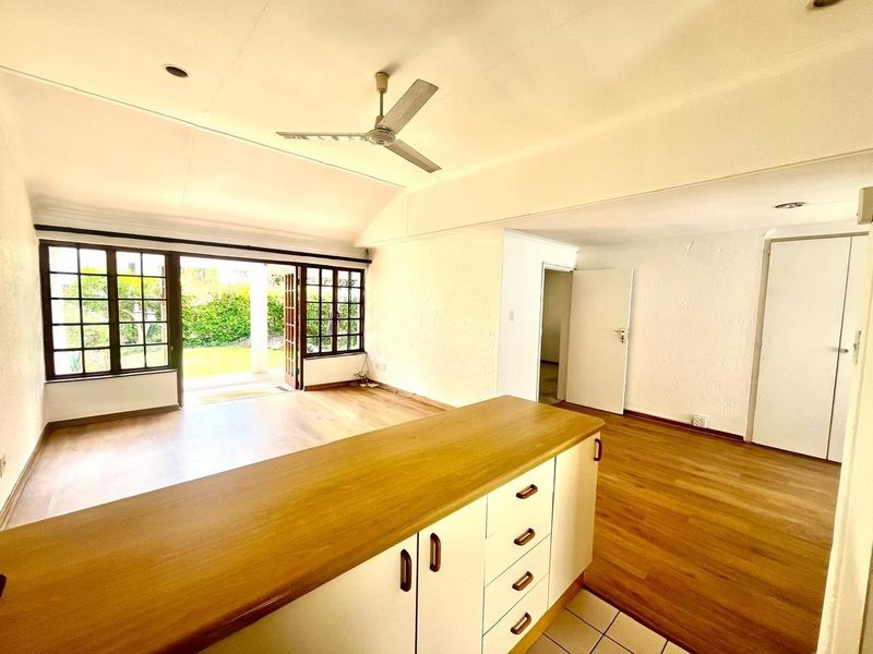 Spacious open-plan living area featuring timber laminate flooring, a central kitchen island with timber countertop, and direct access to the garden through french doors.