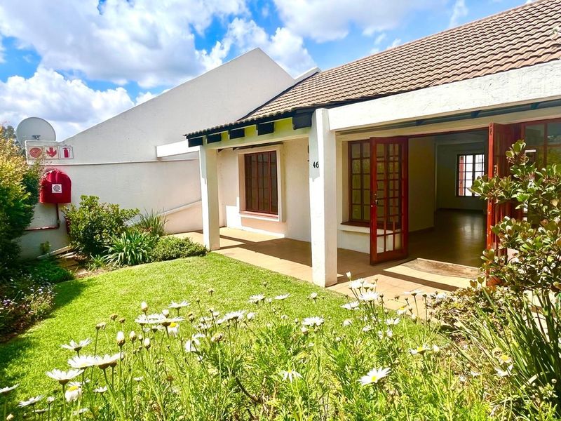 A well-maintained rear exterior view featuring a covered patio, landscaped garden, and classic wooden-framed glass doors leading into the residence.