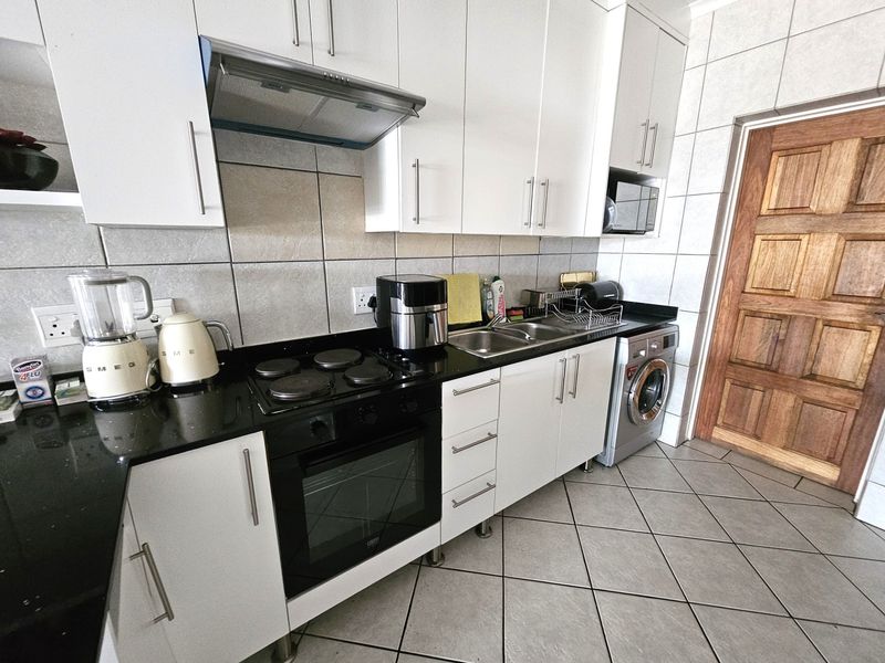 A functional kitchen featuring white cabinetry, black granite countertops, a built-in electric oven and hob, and tiled finishes throughout.