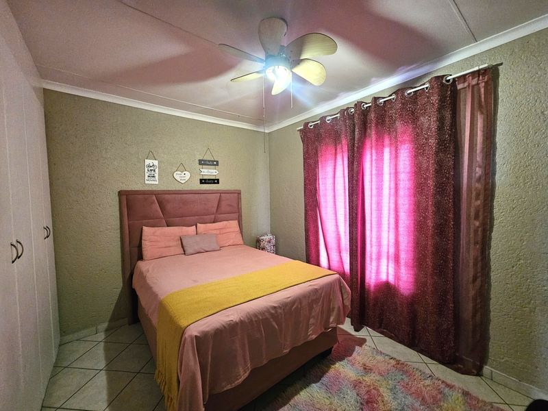 A cozy bedroom featuring built-in cupboards, tiled flooring, and a ceiling fan, offering a functional and comfortable living space.