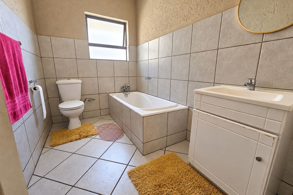 A functional bathroom featuring a built-in bathtub, a vanity with basin, and neutral floor-to-ceiling tiling, providing a clean and practical space.