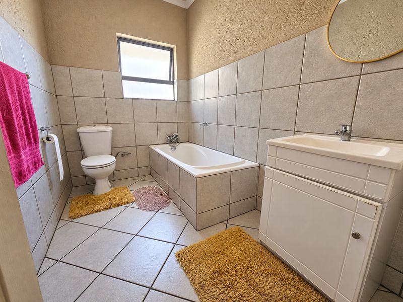 A functional bathroom featuring a built-in bathtub, a vanity with basin, and neutral floor-to-ceiling tiling, providing a clean and practical space.
