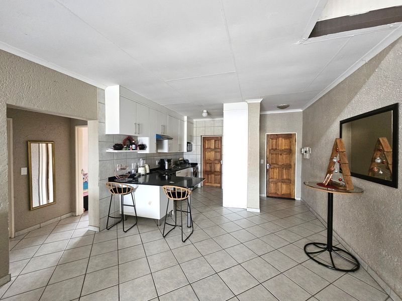 Open plan kitchen and living area featuring tiled flooring, granite countertops, and built-in cabinetry, with direct access to adjacent rooms via timber doors.