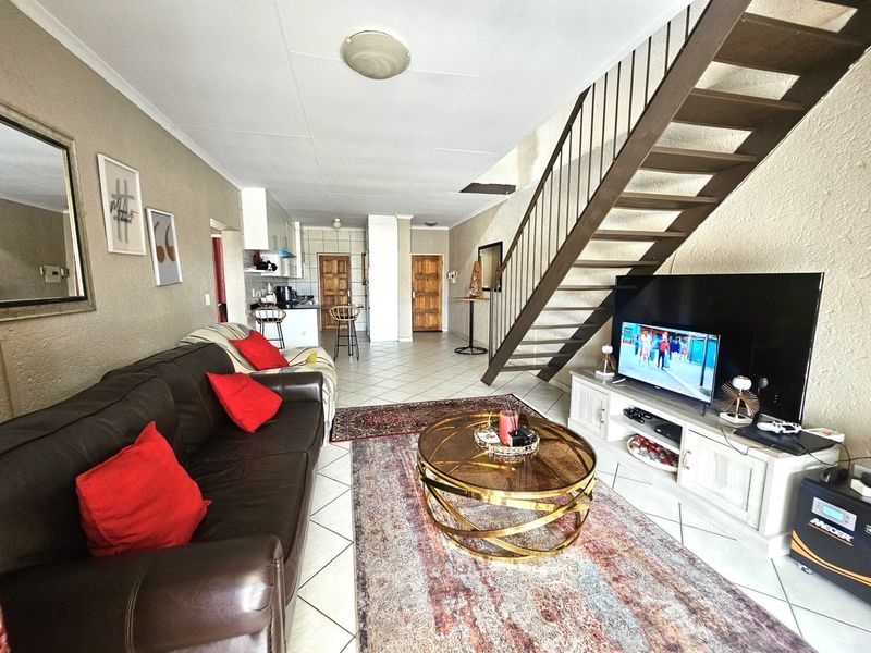 Open-plan living area featuring tiled flooring, a staircase with a metal handrail, and an integrated kitchen space.