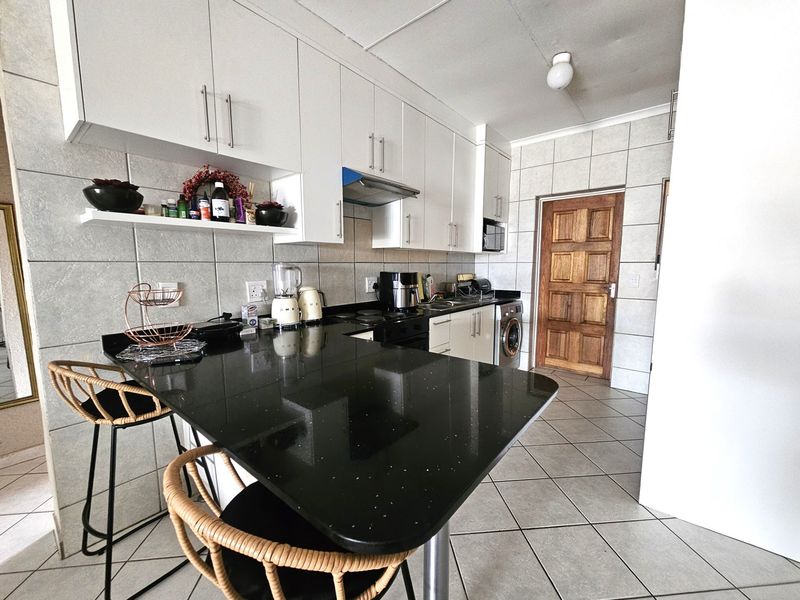 Modern kitchen featuring white cabinetry, black granite countertops, tiled backsplash, and integrated laundry appliances, offering a functional and clean workspace.