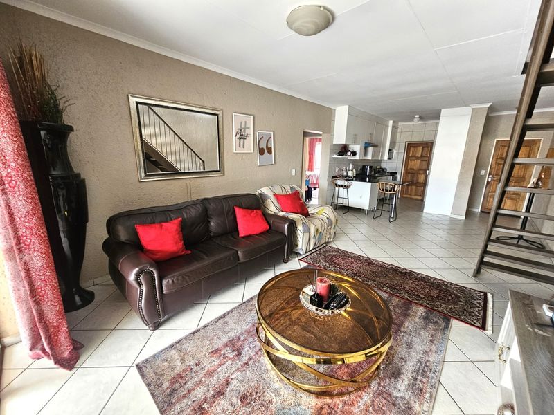 Open-plan living area featuring tiled floors, a functional kitchen with island, and a staircase, offering a versatile layout for modern apartment living.