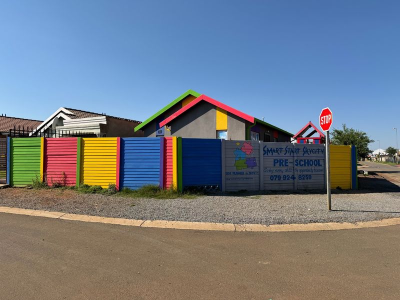 Front exterior view of a brightly painted property currently operating as a pre-school, featuring a colorful perimeter fence and clear street access.