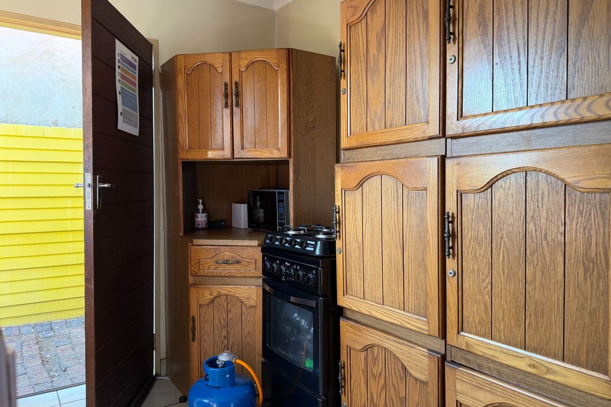 A compact kitchen area featuring traditional wooden cabinetry, a gas stove with oven, and direct access to an outdoor space.