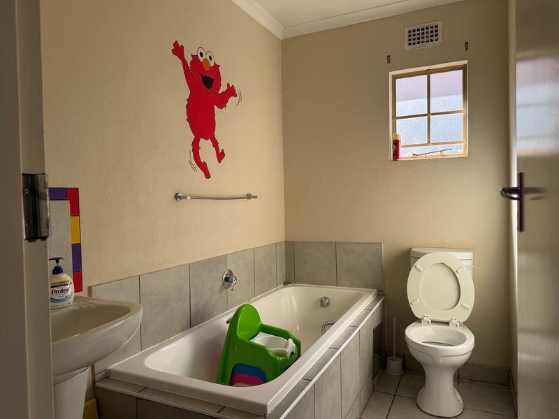 A functional bathroom featuring a built-in bathtub, pedestal basin, and toilet with tiled splashbacks and flooring.