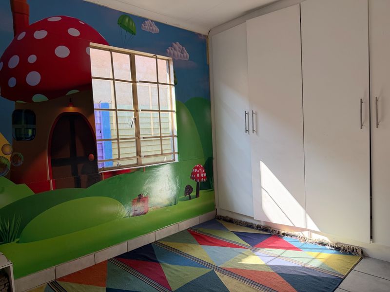 A bedroom featuring built-in cupboards, tiled flooring, and a window with security bars, currently decorated with a mural.