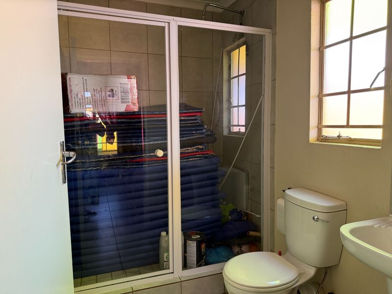 A functional bathroom featuring a shower enclosure, toilet, and washbasin, with tiled walls and a window providing natural light.