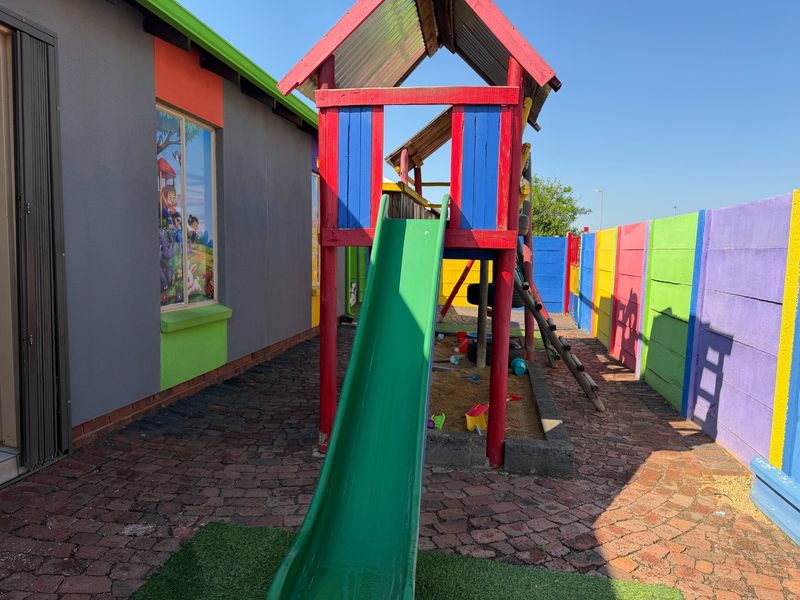 Outdoor play area featuring a paved courtyard, sandpit, and colorful perimeter wall, suitable for a childcare or residential facility.