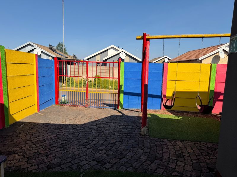 A private outdoor courtyard featuring colorful boundary walls, paved flooring, and a fixed swing set, providing a secure and playful exterior space.