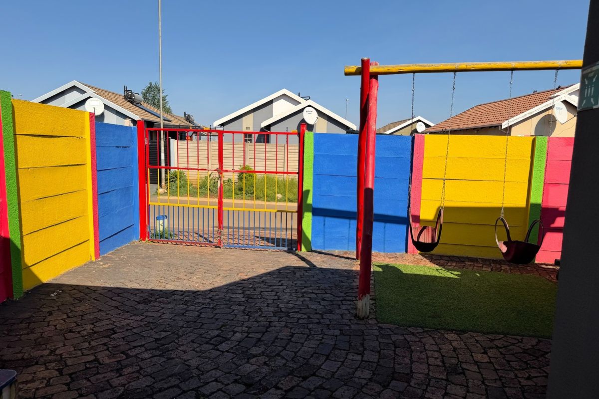 A private outdoor courtyard featuring colorful boundary walls, paved flooring, and a fixed swing set, providing a secure and playful exterior space.