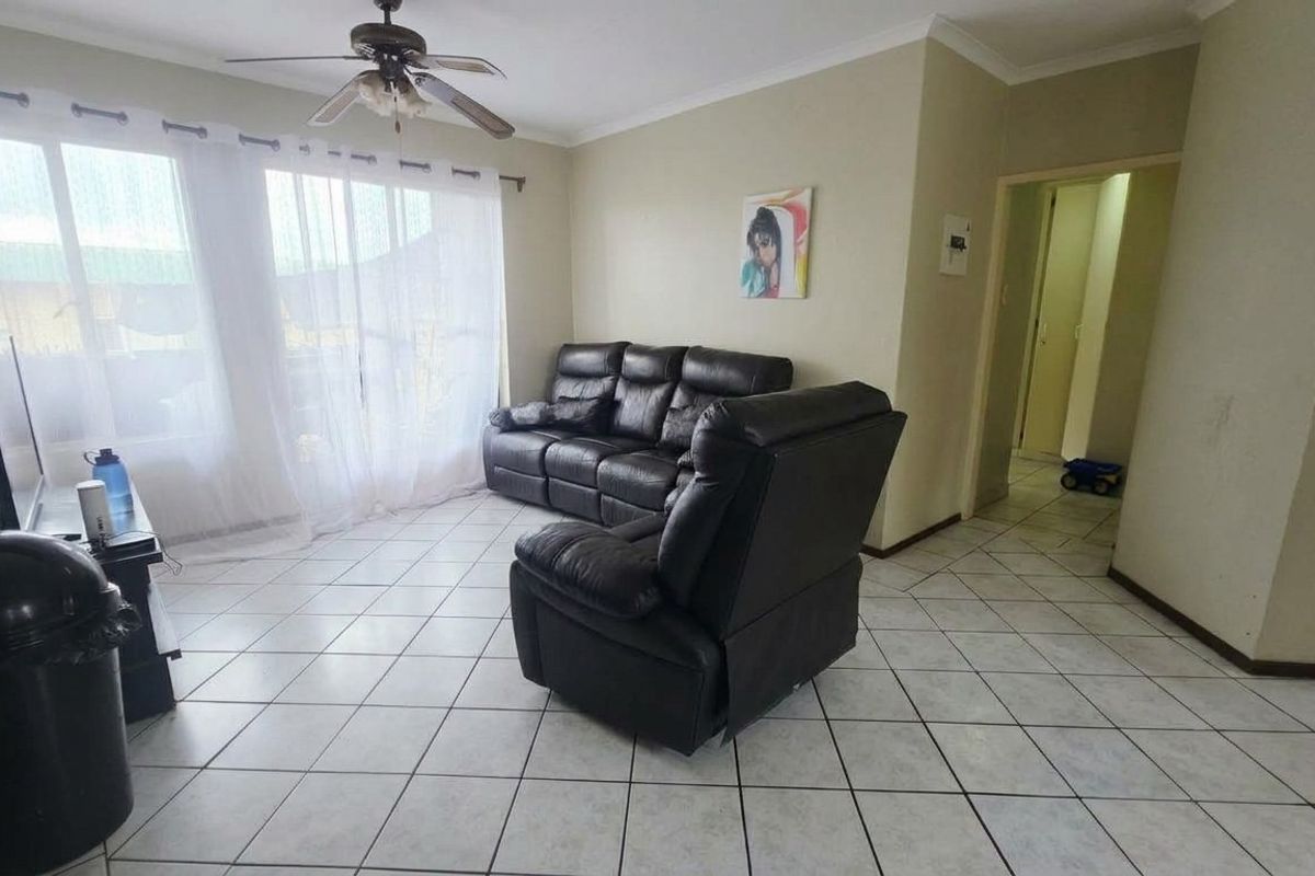A functional living room featuring tiled flooring, a ceiling fan, and a sliding glass door providing natural light.