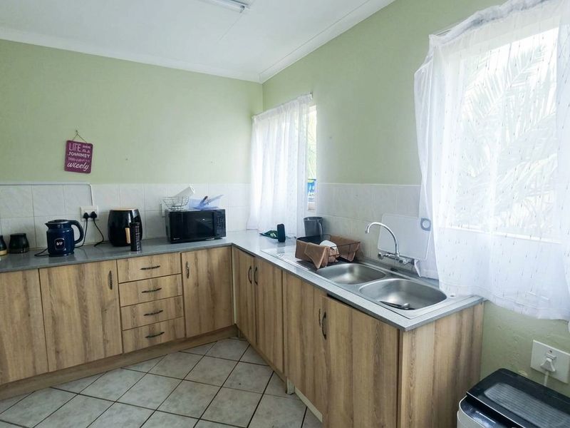 Functional kitchen featuring light wood-look cabinetry, double stainless steel sink, tiled splashback, and ceramic floor tiles.