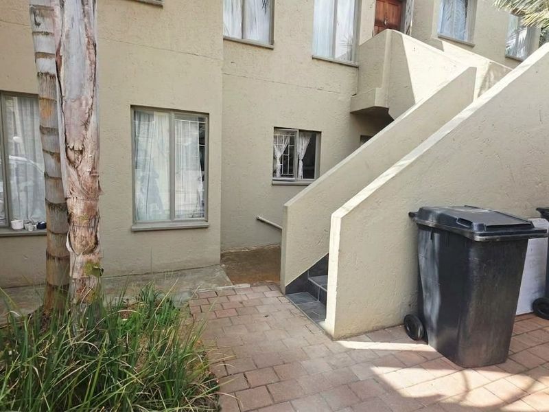 Front exterior view of the townhouse featuring a paved walkway, concrete staircase, and windows fitted with security bars.