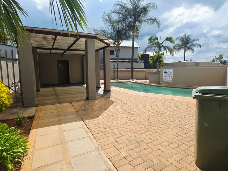 Outdoor pool area featuring a paved deck, a covered patio structure, and perimeter boundary walls in a communal townhouse setting.
