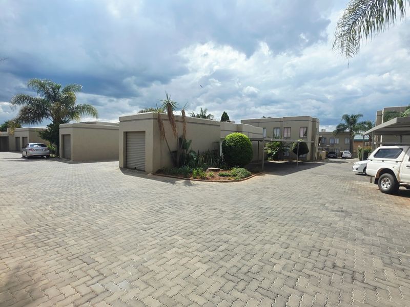 Exterior view of a townhouse complex featuring paved driveways, multiple garage units, and covered carport parking areas.