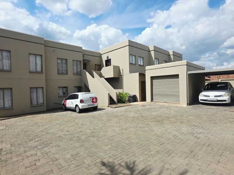 Front elevation of a townhouse complex featuring a paved driveway, covered carport, secure garage, and external staircase access to upper units.