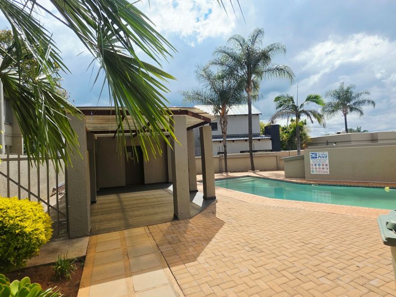 Communal pool area featuring a paved deck, covered patio structure, and perimeter walling within a townhouse complex.
