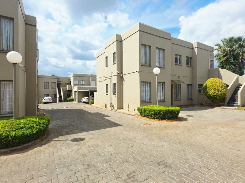 A view of the townhouse complex exterior featuring paved driveways, landscaped hedges, and multi-level residential units with external staircases.