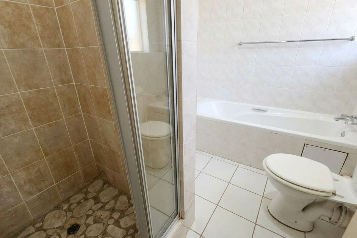 A functional bathroom featuring a separate shower enclosure, bathtub, toilet, and tiled finishes throughout, offering a clean canvas for potential modernization.
