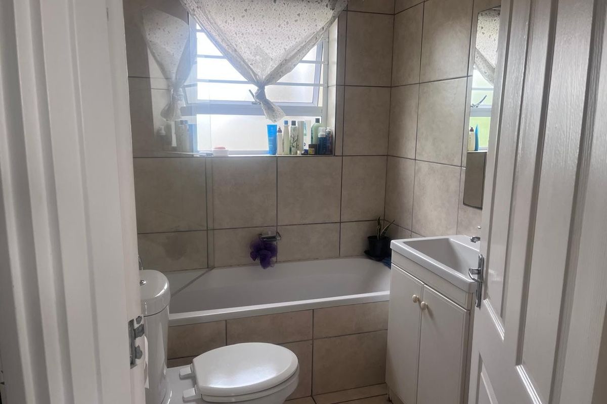 A compact bathroom featuring a bathtub, toilet, and vanity basin with neutral wall and floor tiling.