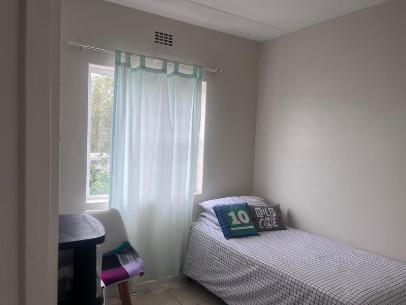 A compact bedroom featuring neutral wall finishes, a window with a curtain rod, and a ventilation grille.