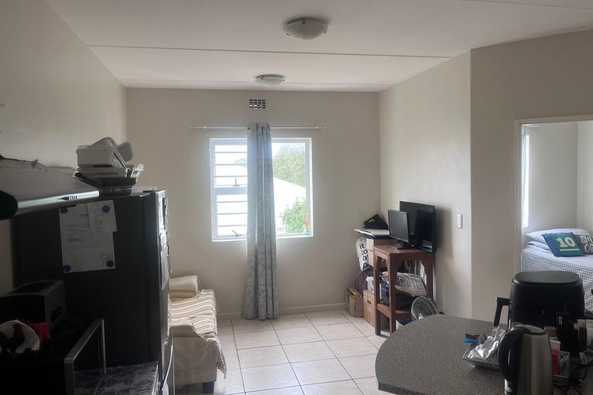 An open-plan living area featuring tiled flooring, a breakfast counter, and a window with security bars, providing a functional and versatile living space.