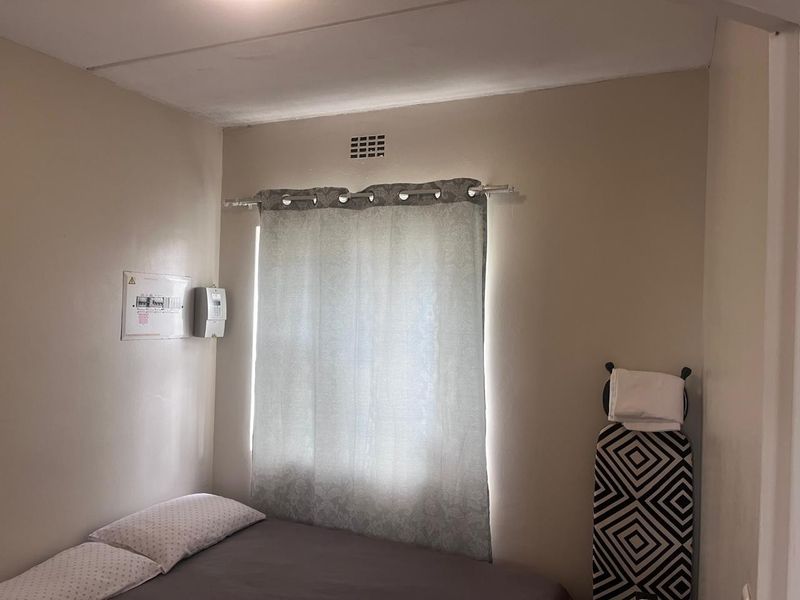 A compact bedroom featuring a wall-mounted electrical distribution board and a ventilation air brick above the window.