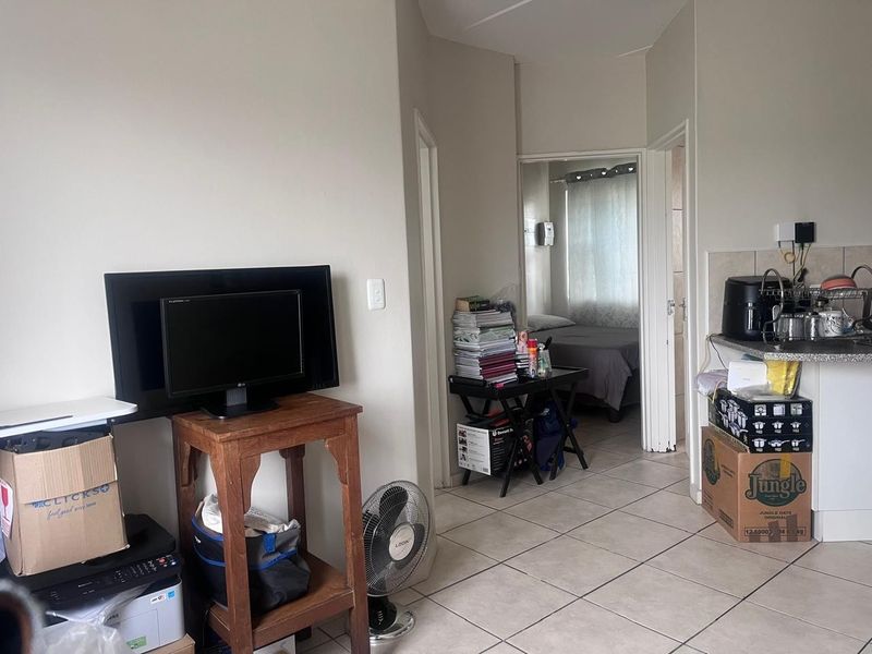 Open plan living area featuring tiled flooring and a compact kitchen corner with counter space and backsplash.