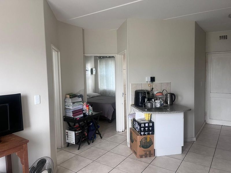 Open plan living area featuring tiled flooring and a compact kitchenette counter, with direct access to an adjacent bedroom.