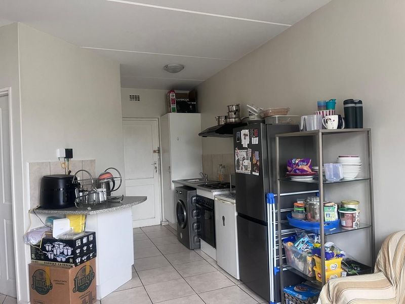 A functional kitchen area featuring tiled flooring, built-in cabinetry, a stove with an extractor fan, and a compact countertop workspace.