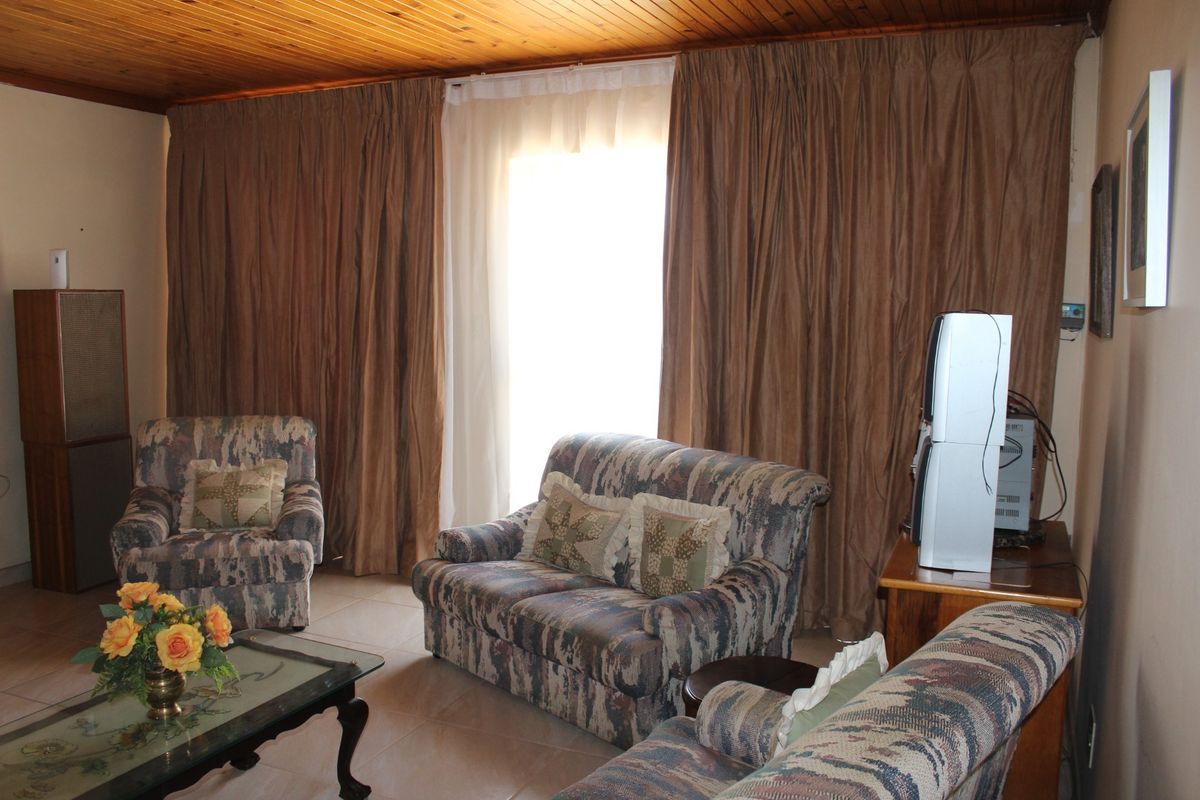 A living room featuring tiled flooring and a timber tongue and groove ceiling, with access to the outdoors via a sliding glass door.