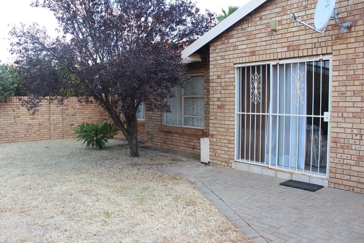 Rear exterior view of the townhouse featuring a face brick facade, paved patio area, and a secure sliding door entrance.
