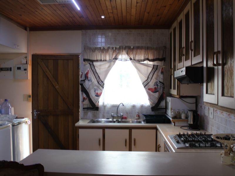 A dated kitchen featuring timber ceilings, built-in cabinetry, a gas hob with extractor fan, and a double sink with tiled backsplash.