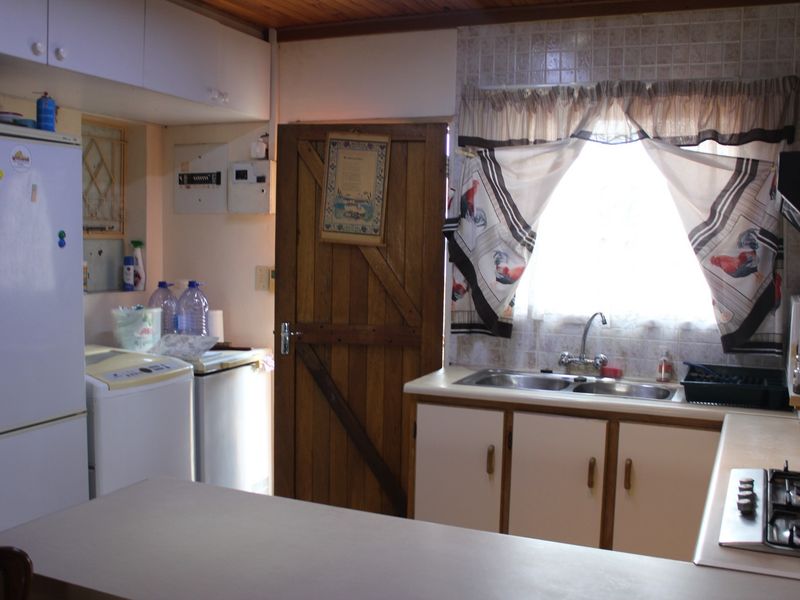 A functional kitchen featuring built-in cabinetry, a double sink, gas hob, extractor fan, and a timber ceiling, offering potential for modernization.